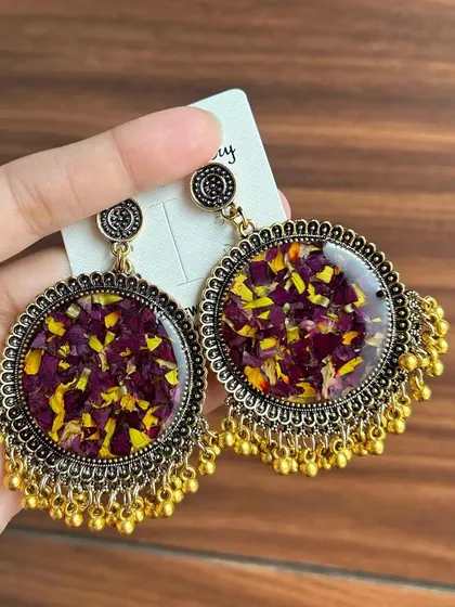 A pair of large, round resin earrings with preserved flower petals inside. The antique gold finish and ghungroo details give them a traditional look.