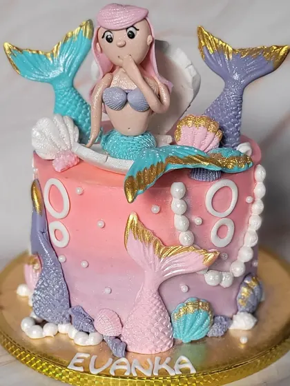 A fun and colorful mermaid theme cake. The pink and purple ombre buttercream is decorated with mermaid tails, seashells, and a cute mermaid topper.