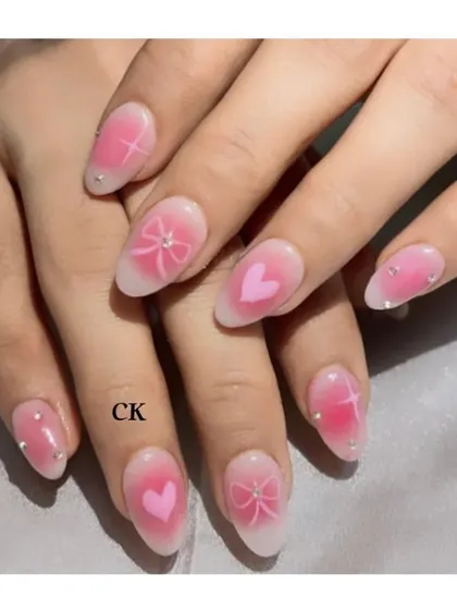 A close-up of the trendy airbrush nails, featuring a soft pink heart and bow design over a white ombré base.