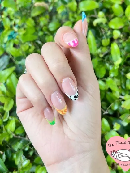 A playful and colorful set of almond nails with a mix of designs, including multi-colored French tips and cow print accents.