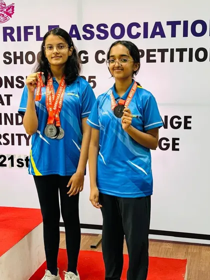 Indu and Bhuumika, two of our decorated air rifle athletes, standing together with their medals after a successful state-level competition.