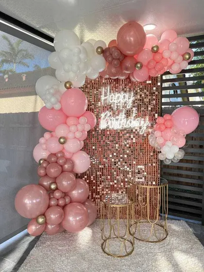 A beautiful rose gold themed birthday party. A shimmer wall is decorated with an organic balloon garland in various shades of pink, with elegant gold plinths for the cake.