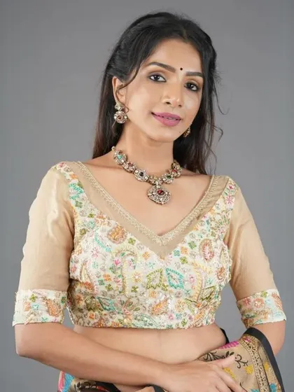 This model wears a cream-colored blouse with delicate multi-color embroidery, paired with a matching antique-finish necklace.