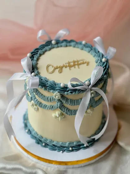 A beautiful "Congratulations" cake in a dusty blue and white palette. The vintage Lambeth piping and white ribbons give it a classic and celebratory feel.