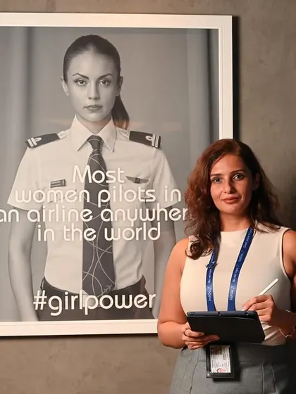 An IndiGo employee standing next to a poster celebrating the airline's female pilots. This is a powerful image for corporate social responsibility and employer branding.