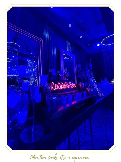 A moody and sophisticated cocktail bar setup, using deep blue lighting and neon signs to create a chic, lounge-like atmosphere perfect for evening events and sangeets.