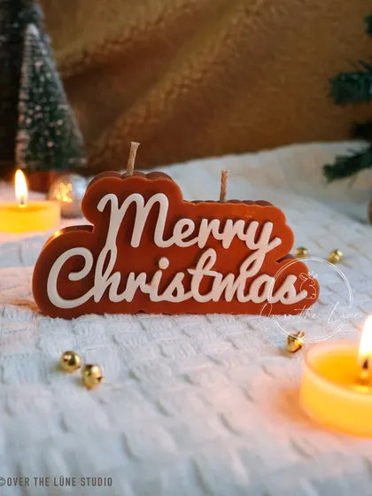 The 'Merry Christmas' candle in a warm, gingerbread-brown color. This version has a cozy, rustic feel, perfect for a farmhouse Christmas theme.
