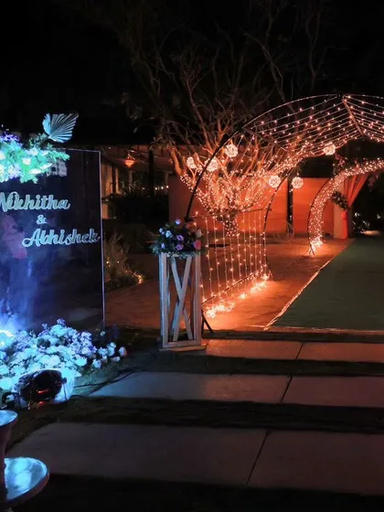 A personalized entrance featuring a mirrored sign with the couple's names, flanked by floral arrangements. The fairy light tunnel in the background promises a magical celebration ahead.