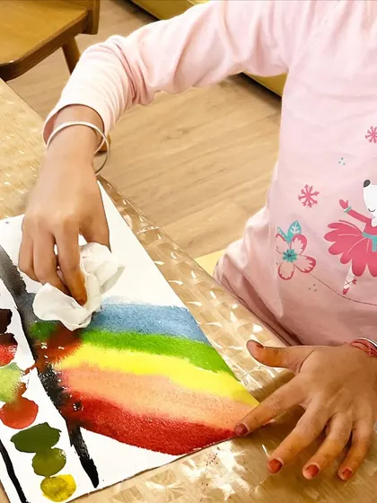 A young girl carefully creates a vibrant rainbow with watercolors. This simple activity allows for exploration of color theory and blending in a free and expressive way.
