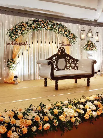 A beautiful ring ceremony stage with a floral arch of peach and white roses. The couple's names are displayed in a custom cutout, and hanging Edison bulbs add a warm, rustic-chic touch to the decor.