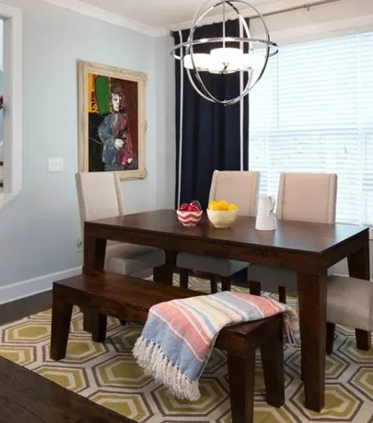A casual dining space with a mix of chairs and a bench, a geometric-patterned rug, and a modern spherical chandelier.