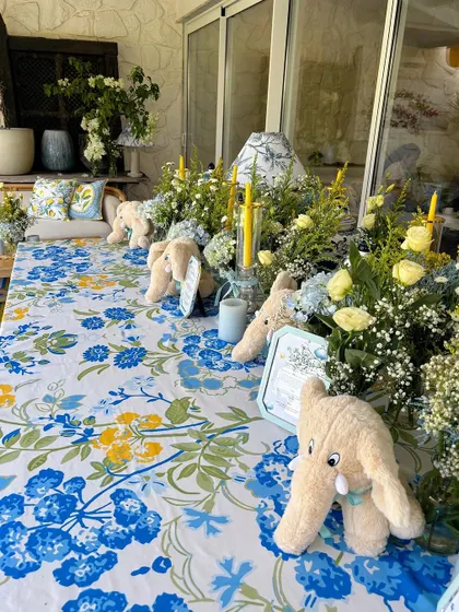 A long table decorated with a blue and yellow floral tablecloth, plush elephant toys, and arrangements of baby's breath.