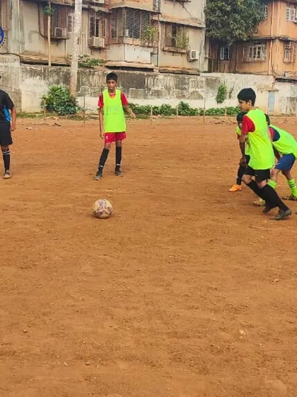 Kicks, goals, and grit. A young player in a neon bib focuses on the ball during a practice match on a dirt field, representing the starting point of every champion's journey.