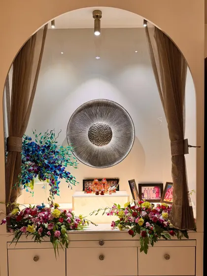 A tranquil prayer and devotion nook designed within a living area. The space is framed by a simple arch and soft curtains, with a hammered metal art piece serving as a spiritual focal point. It’s a perfect example of integrating sacred spaces into daily life.