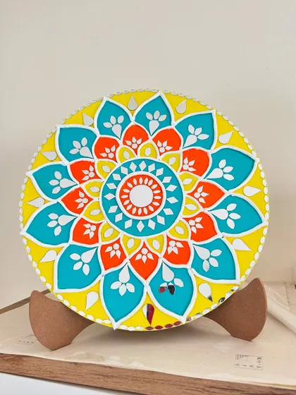 A bright and cheerful Lippan art piece with a yellow, orange, and teal floral design, displayed on a stand.