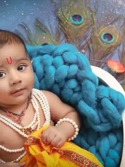 With a curious gaze, this baby embodies the spirit of Kanha. The vibrant peacock feathers and rich blue textures create a stunning and memorable portrait.