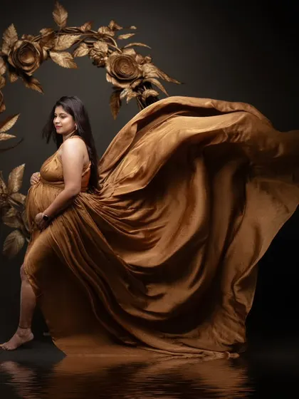 Some moments are beyond words. This radiant mom-to-be is draped in elegance, with a dramatic flowing gown and a golden floral heart backdrop.