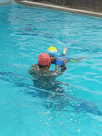 A coach provides hands-on support to a toddler, ensuring they feel secure while learning to kick in the water.