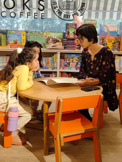 Small group interactions make our reading sessions special. Here, a storyteller engages with two young readers, discussing the book and answering their curious questions.
