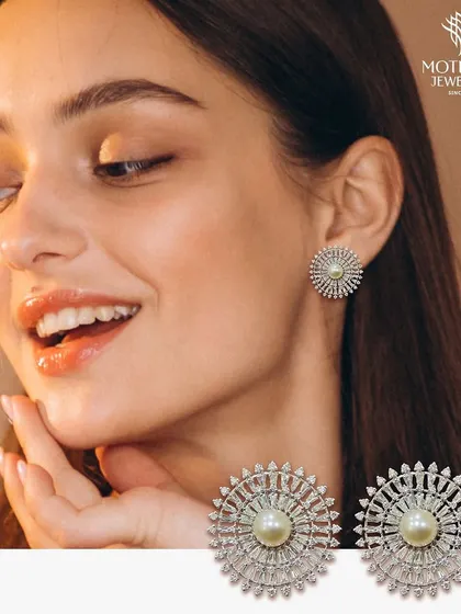 A beautiful pair of stud earrings featuring a central pearl surrounded by a halo of radiating baguette diamonds. The design is reminiscent of a celestial starburst.
