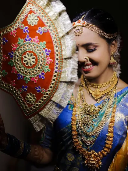 A joyful bridal portrait, where the bride smiles while holding a traditional embroidered fan, a unique element of her attire.