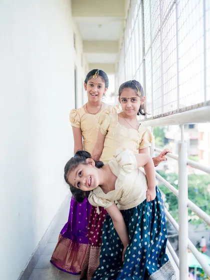 Three young girls in traditional outfits share a playful moment on a balcony during a family event. We capture the fun side of formal occasions.