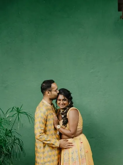 A candid moment from a haldi ceremony, with the couple sharing a happy, intimate moment against a vibrant green wall.