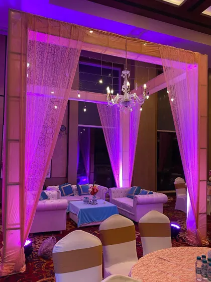 An indoor lounge area for a wedding event, with comfortable sofas set under a simple canopy with a chandelier. Perfect for guests to relax.