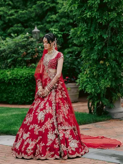 A quiet moment of reflection before the ceremony. This full-length view showcases the magnificent flare and detailed craftsmanship of her traditional red bridal lehenga.