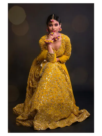 A full-length shot of a model in a beautiful yellow lehenga. The bokeh background adds a festive and magical touch.
