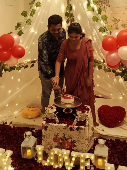 A happy couple cutting their anniversary cake inside the cozy canopy tent I set up for them. The scene is filled with rose petals, lanterns, and "LOVE" marquee letters, making for a perfect celebration.