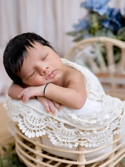A close-up of a sleeping newborn, resting peacefully in a lace-draped wicker basket. The textures of the lace and basket add a beautiful rustic touch.