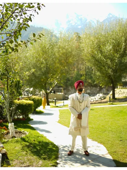 The groom, Rishi, standing in the lush gardens of the Manali wedding venue. The snow-capped mountains in the background add a majestic touch to this outdoor groom portrait.