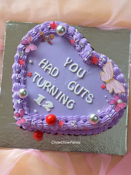 A vintage-style heart cake inspired by Olivia Rodrigo's "Guts" album. This Chocolate Raspberry cake is decorated with purple buttercream piping, butterflies, and silver details.