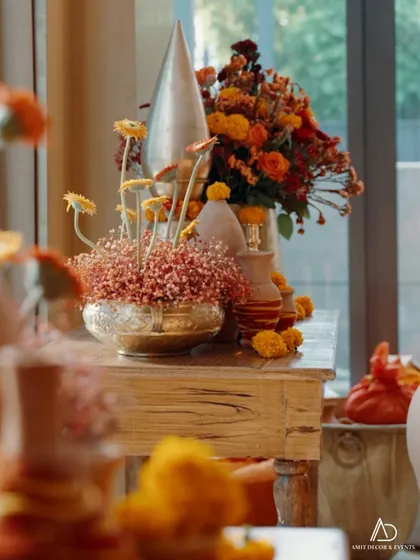 A warm and inviting corner with traditional decor, showcasing a mix of marigolds and other flowers in brass bowls and vases on a rustic wooden table.
