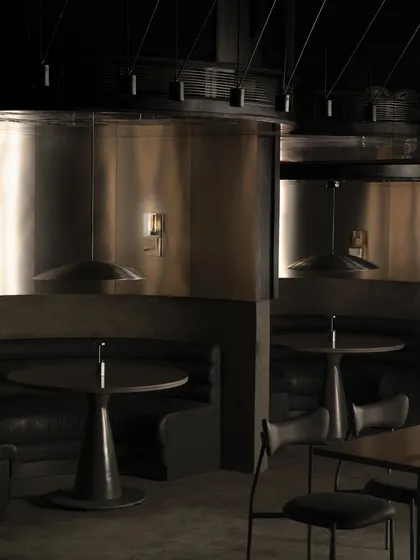 The main dining area of Lair, where curved metal partitions create semi-private booths. The reflective surfaces create a disorienting yet captivating play of light and shadow.