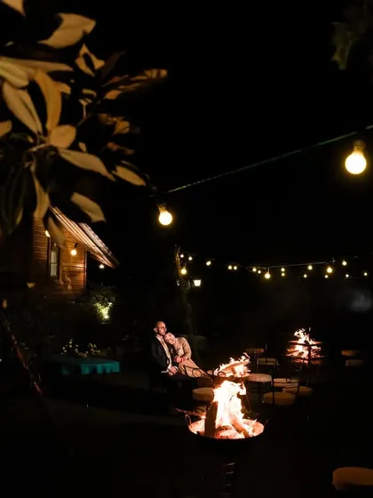 A wide shot of the couple by the bonfire, showing the entire setup with string lights. This photo captures the cozy and rustic ambiance of their celebration.