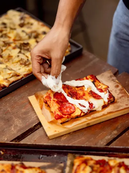 A chef adds fresh burrata to a slice of our square Pizza Romana. This style of pizza has a thicker, focaccia-like base that's light and airy.