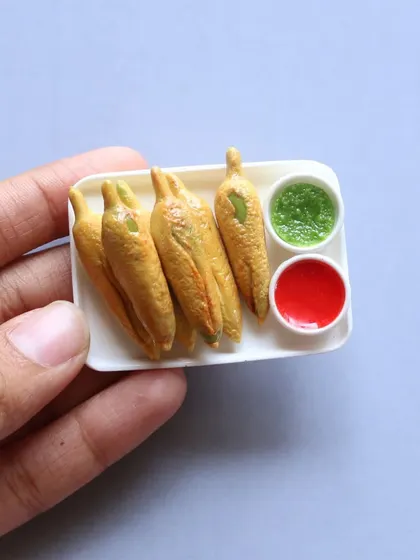 A miniature of mirchi bajji (chili fritters) with green and red chutneys.