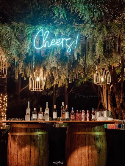A simple yet stylish rustic bar setup for a cocktail evening. I used wooden barrels as the base and hung bamboo cage lights from the trees, topped with a "Cheers!" neon sign to get the party started.