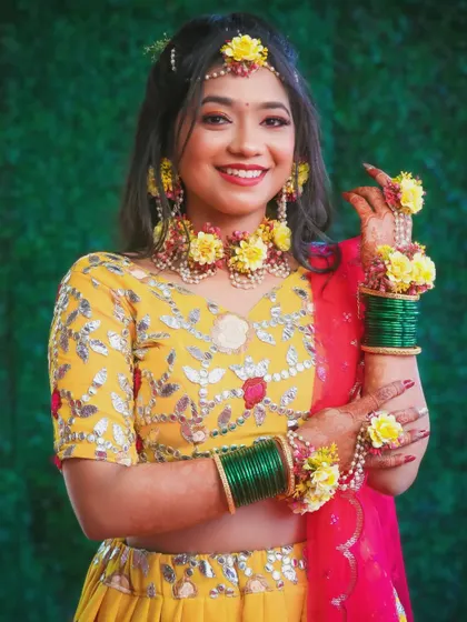 A bride ready for her Haldi or Mehendi ceremony, adorned with beautiful floral jewellery that matches her yellow outfit.