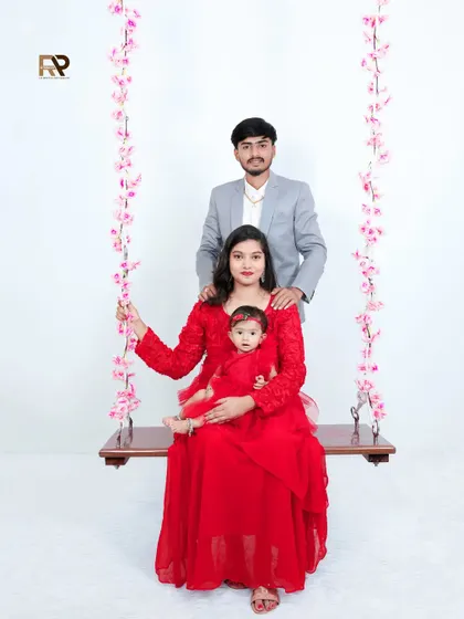 A lovely family portrait with mom and dad sitting on a floral swing with their baby girl. The matching red outfits create a cohesive and visually striking image.
