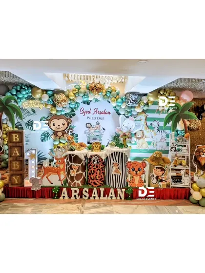 A grand jungle theme for Syed Arsalan's first birthday. The stage is packed with details, including a zebra, deer, and monkey cutouts, 'BABY' blocks, and a backdrop filled with friendly animal faces.