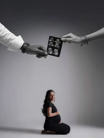 A creative and artistic composition. The parents' hands hold the sonogram above the mother-to-be, symbolizing their joint love and protection over their growing family.