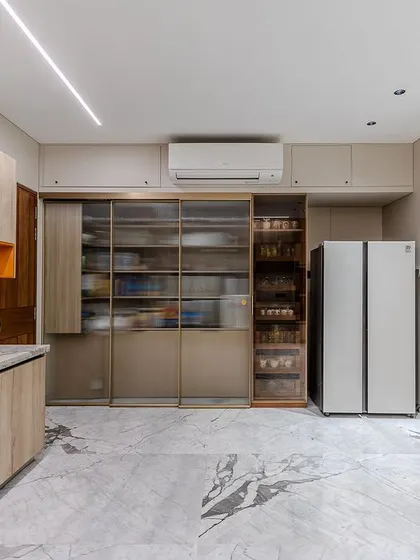 In Dr. Sneha Baxi's Ahmedabad kitchen, a large pantry unit with sliding glass doors and internal pull-outs offers incredible storage capacity and organization.