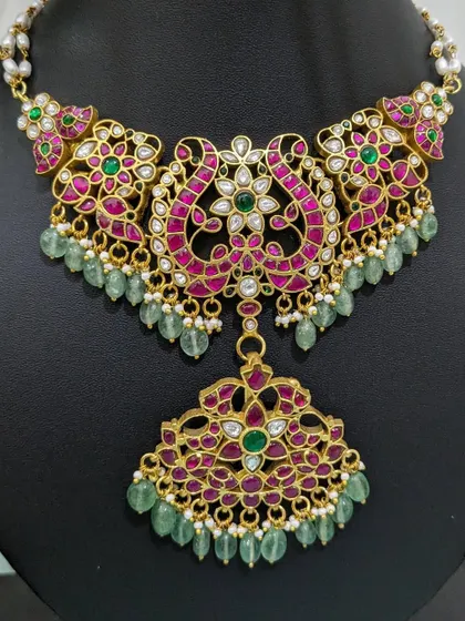 A close-up of an intricate Jadau choker with a floral pendant and green strawberry beads.