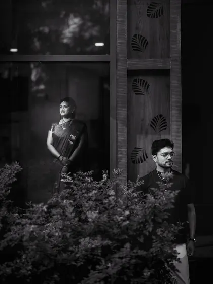 An artistic black and white portrait using reflections and natural elements. The couple is captured in separate but connected frames, suggesting two individuals coming together as one.