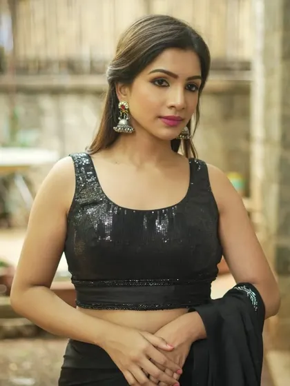 A model wears silver-toned jhumkas with a simple dome shape. This is a versatile piece that pairs well with both modern and traditional outfits, as shown with her sequined blouse.