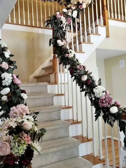 A lush floral garland made of pink, white, and deep red flowers beautifully wrapped around a staircase banister. This is a great way to decorate the entire home for a wedding.