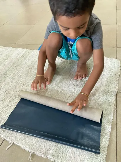 A close-up of a child's hands as he rolls a mat, showing the concentration and dexterity involved in this fundamental Montessori practical life exercise.